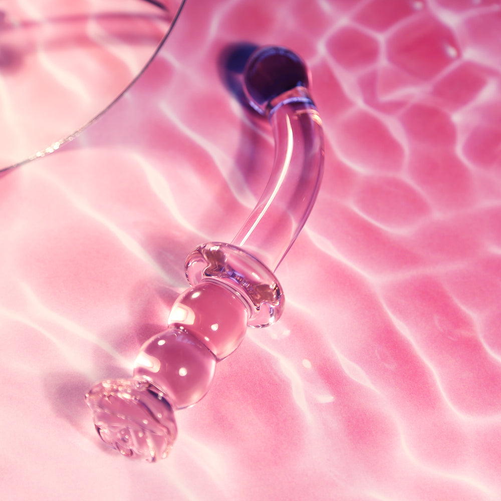Glass G-spot dildo, rosebud detail, on pink background.