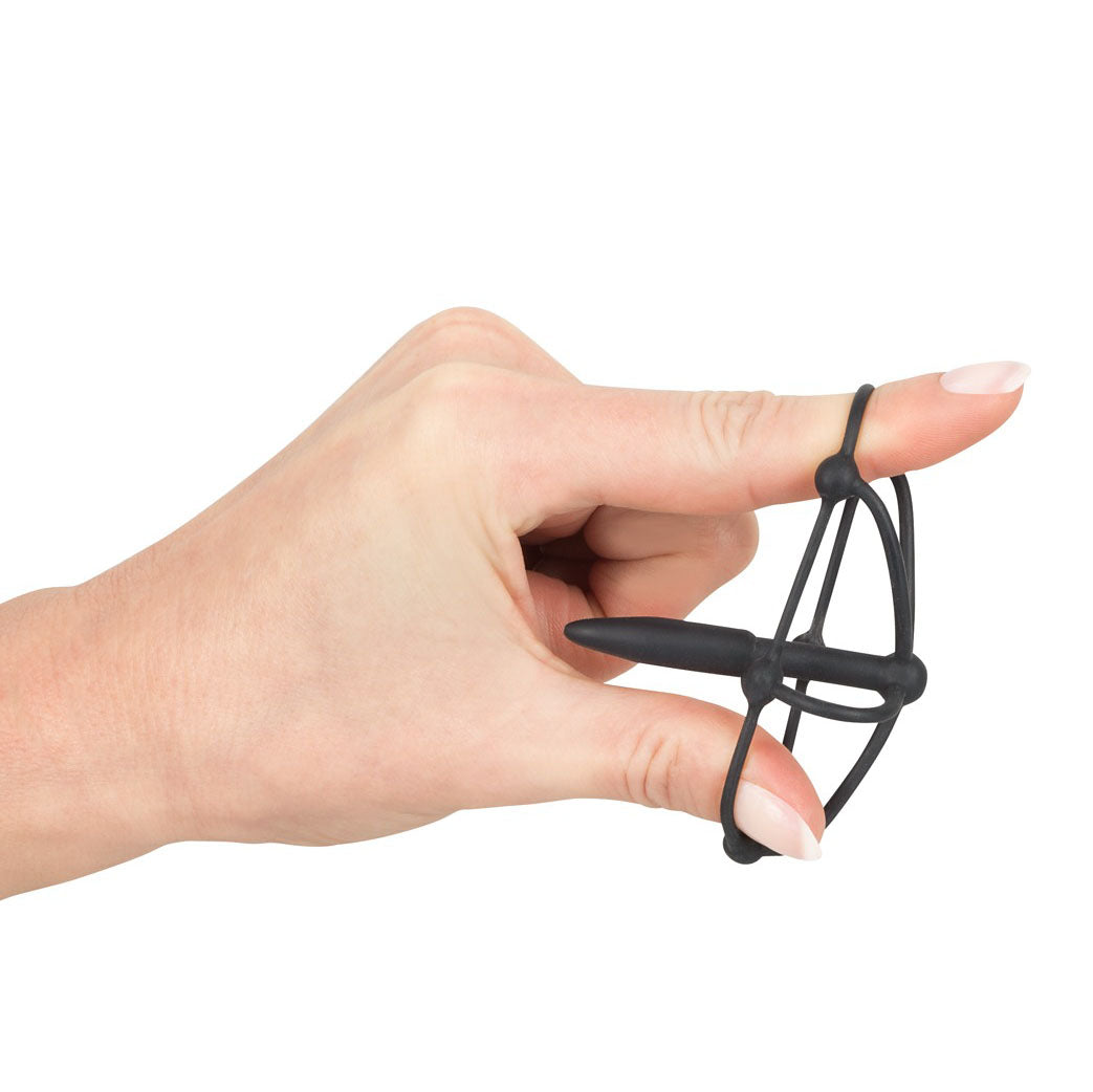 Black silicone penis plug with glans cage held between a finger and thumb.