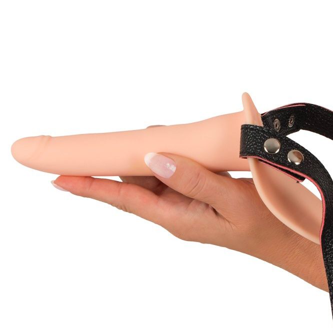 Vibrating strap-on with adjustable harness held in a hand.