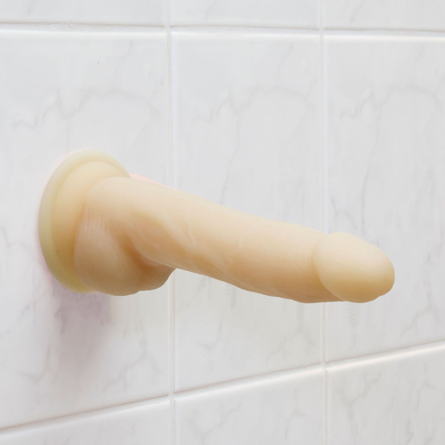 Naked Addiction suction-cup dong against tiled wall.