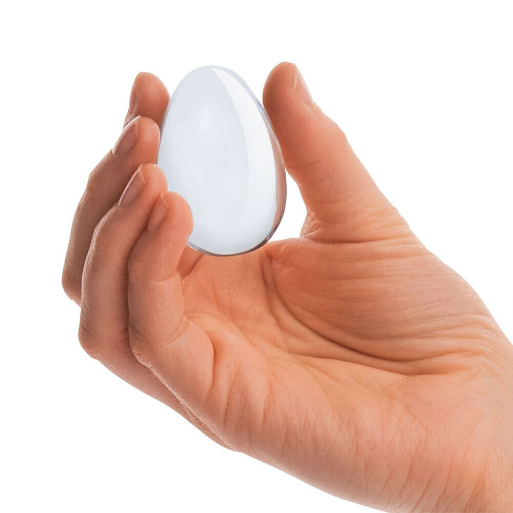 Hand holding a smooth, clear glass yoni egg.