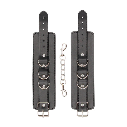 Pair of black leather wrist restraints with connecting chain.