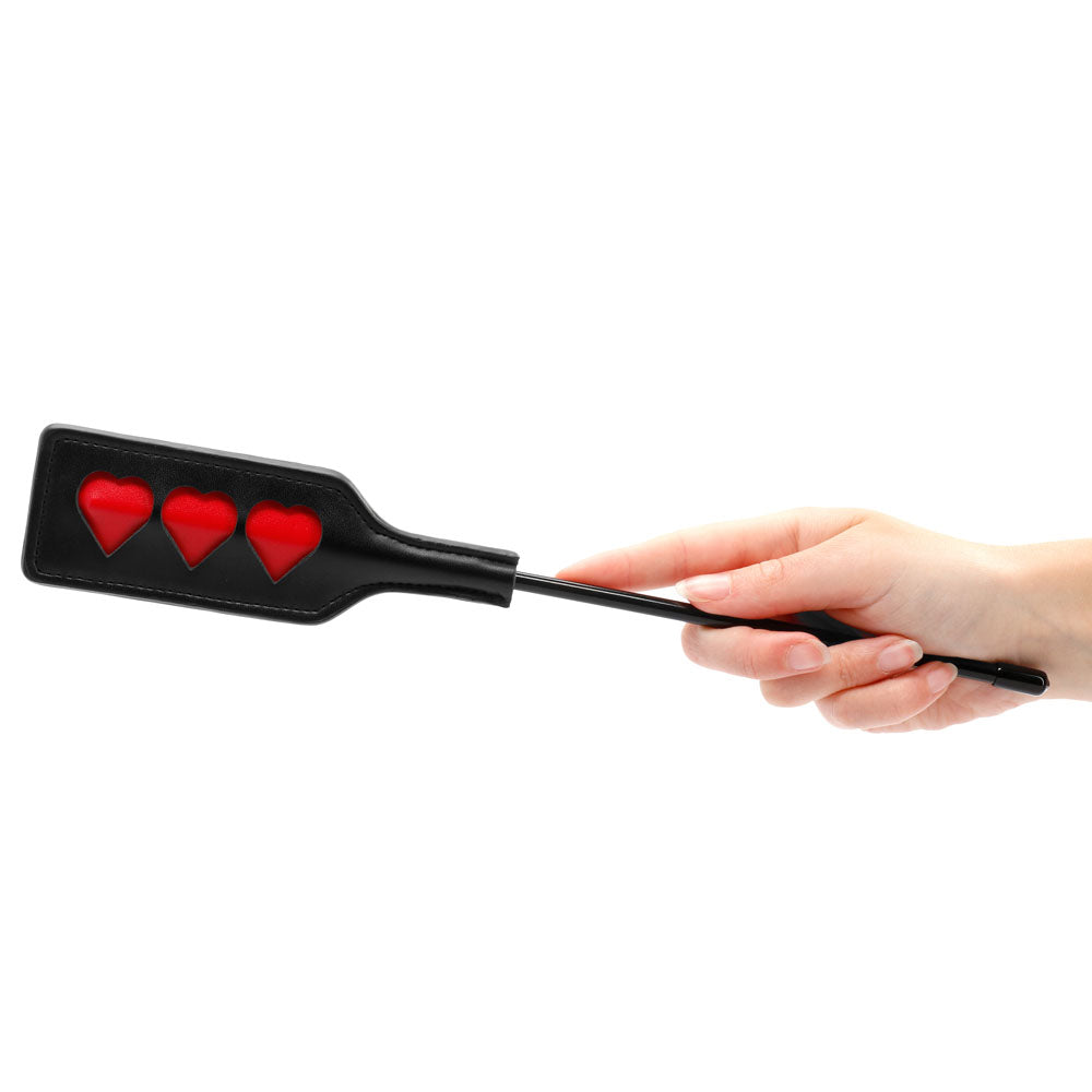 Hand holding a black paddle with red hearts.