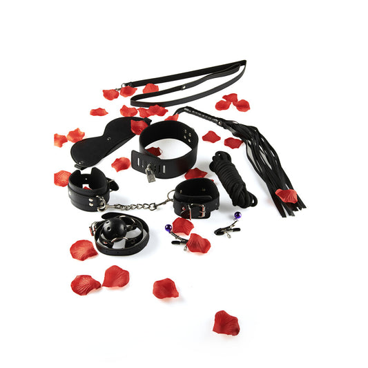 ToyJoy BDSM starter kit with leather restraints, gag, crop, rope and nipple clamps, scattered with rose petals.