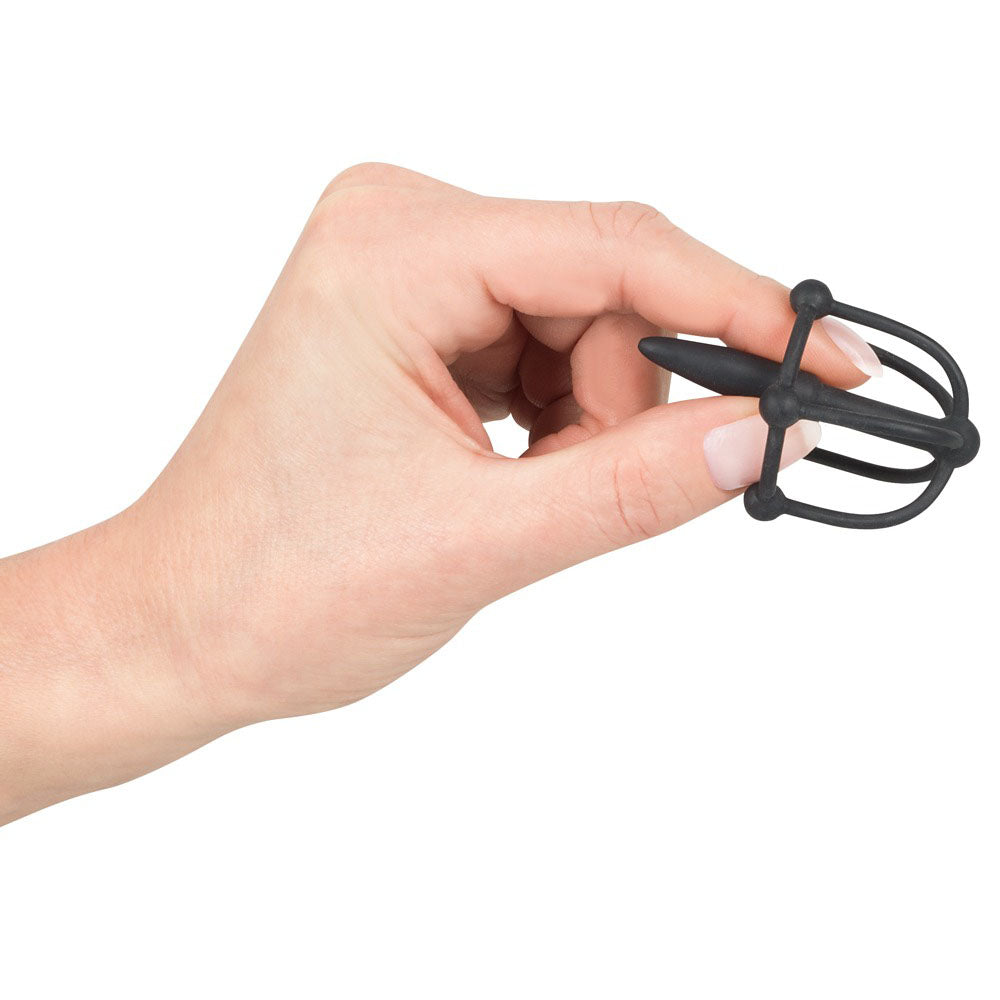 Hand holding a black silicone penis plug with glans cage