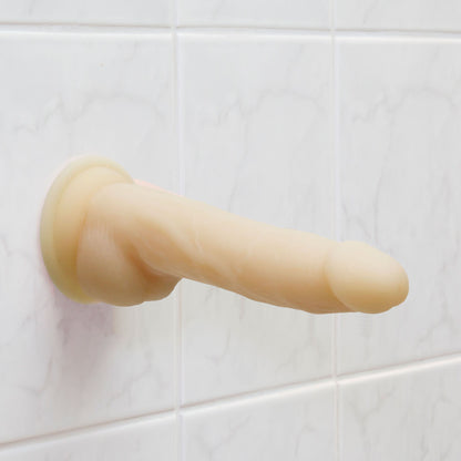 Naked Addiction suction-cup dong against tiled wall.