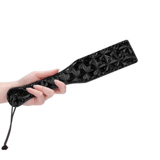Hand holds sleek black Ouch paddle from Shots Toys.