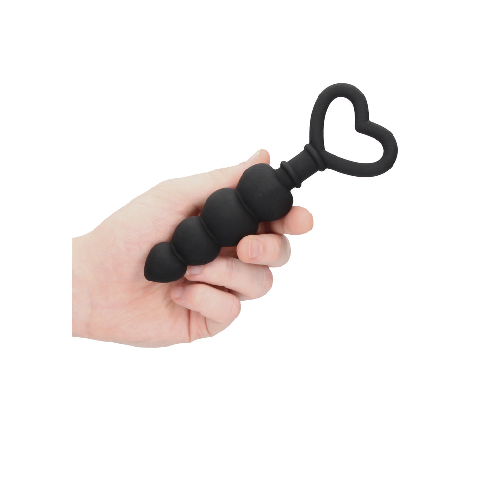 Black silicone anal beads with a heart-shaped handle held in a hand.