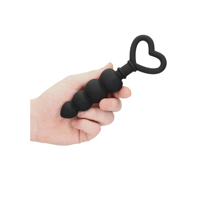 Black silicone anal beads with a heart-shaped handle held in a hand.