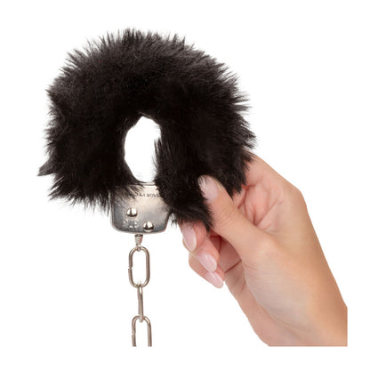 Black furry handcuffs held by a hand.